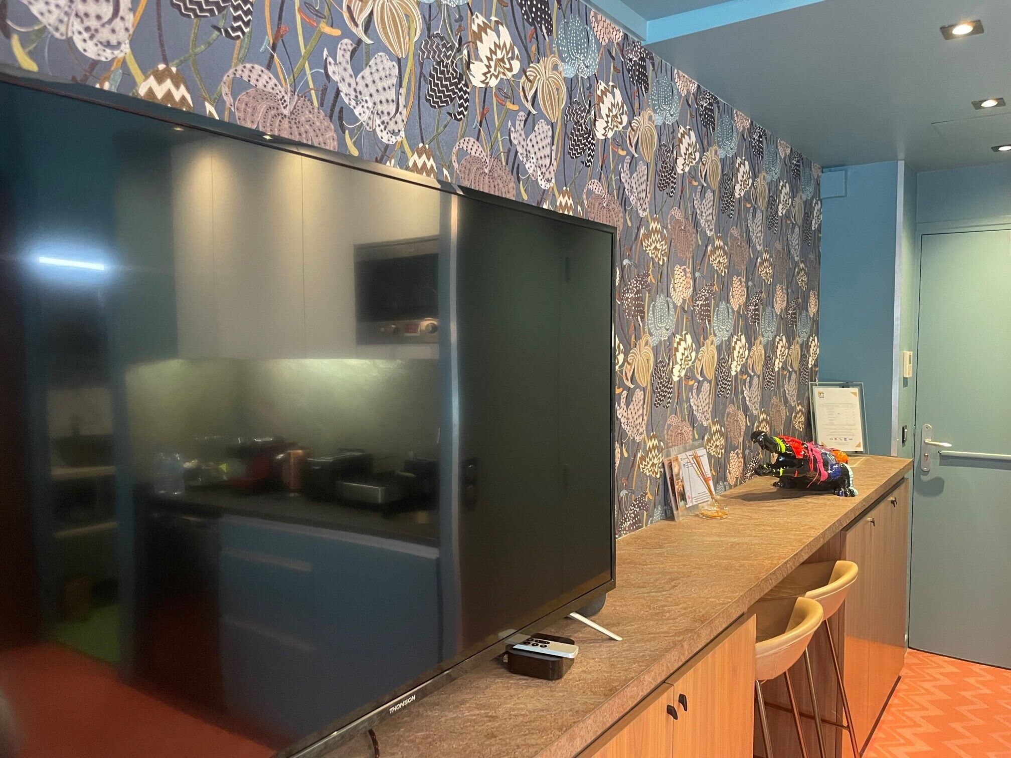 Una cocina moderna con un refrigerador grande, un televisor de pantalla plana y una barra con taburetes.