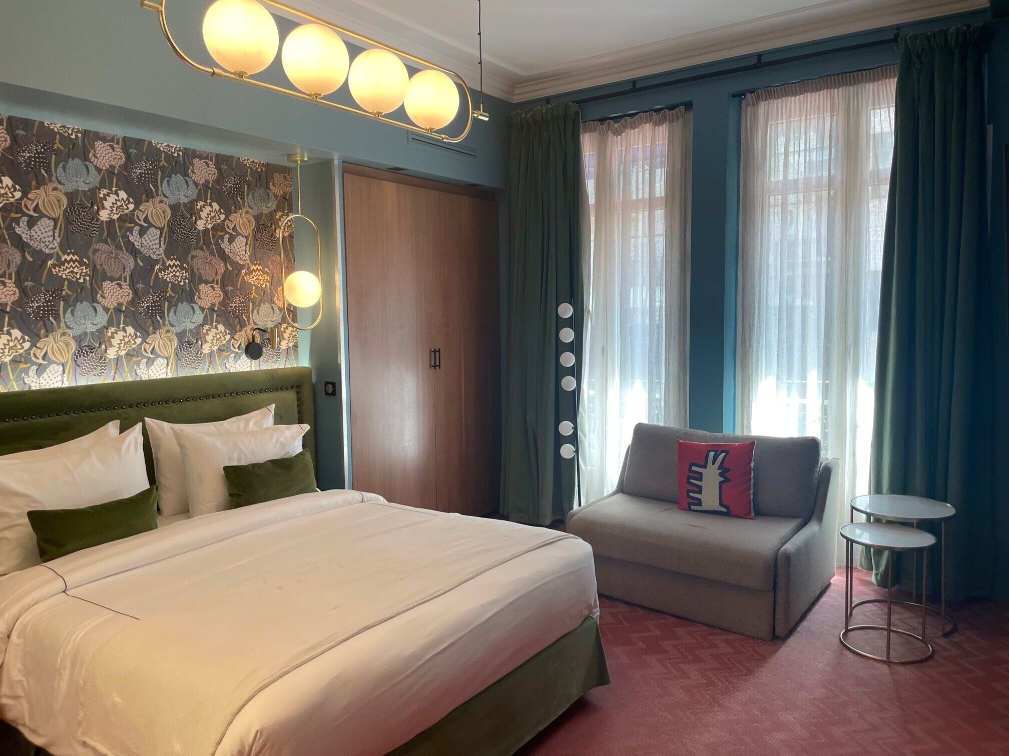 A hotel room with a large bed, a sofa, a small table, and a decorative wall with floral patterns.