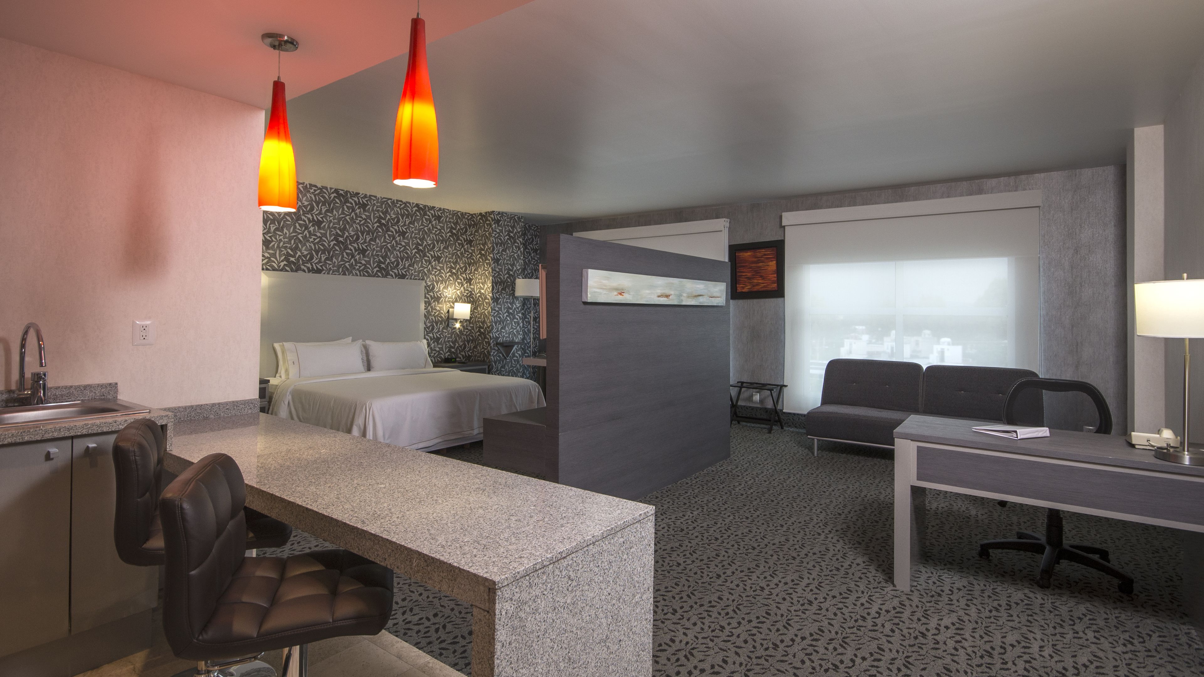 A hotel room with a bed, a desk, a chair, a sofa, and a window with a view.