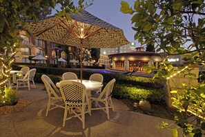 Een terras met rieten stoelen en een patroonbeslagen parasol, een zwembad en een gebouw met een bord waarop Holiday Inn Express & Suites staat.