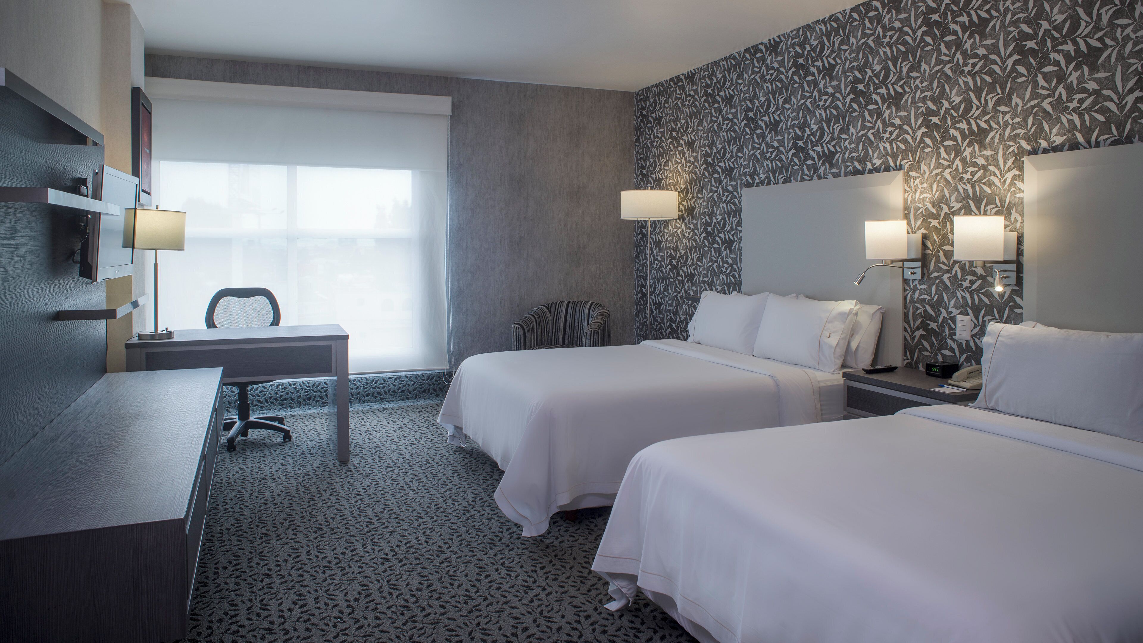 Une chambre d’hôtel avec deux lits, un bureau, une chaise et une grande fenêtre.