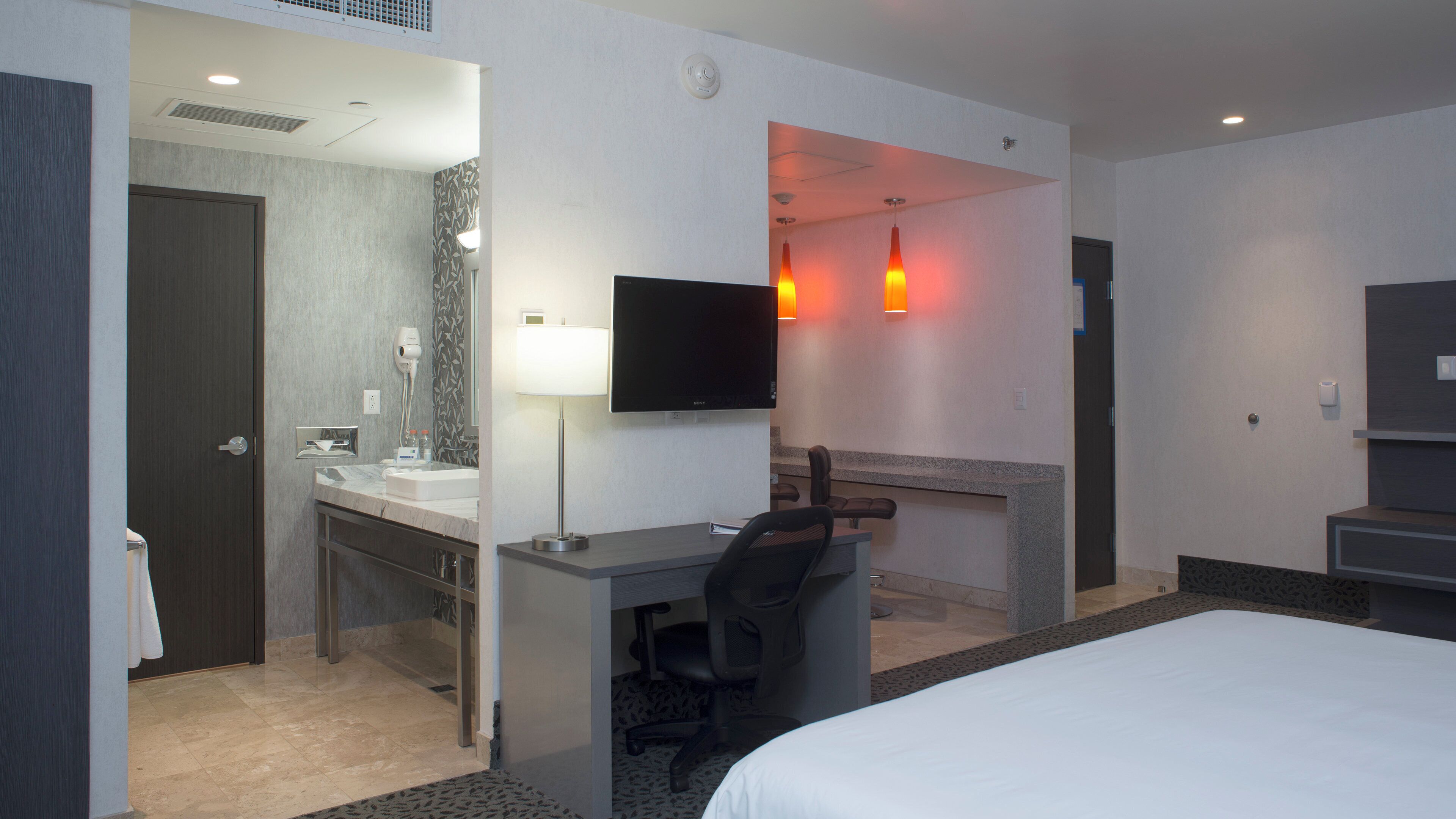 Habitación de hotel con cama, escritorio, silla, televisor y artículos de baño.