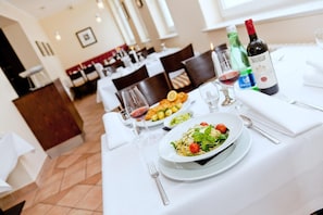 Una mesa de comedor dispuesta con un plato de pasta, una botella de vino y copas.
