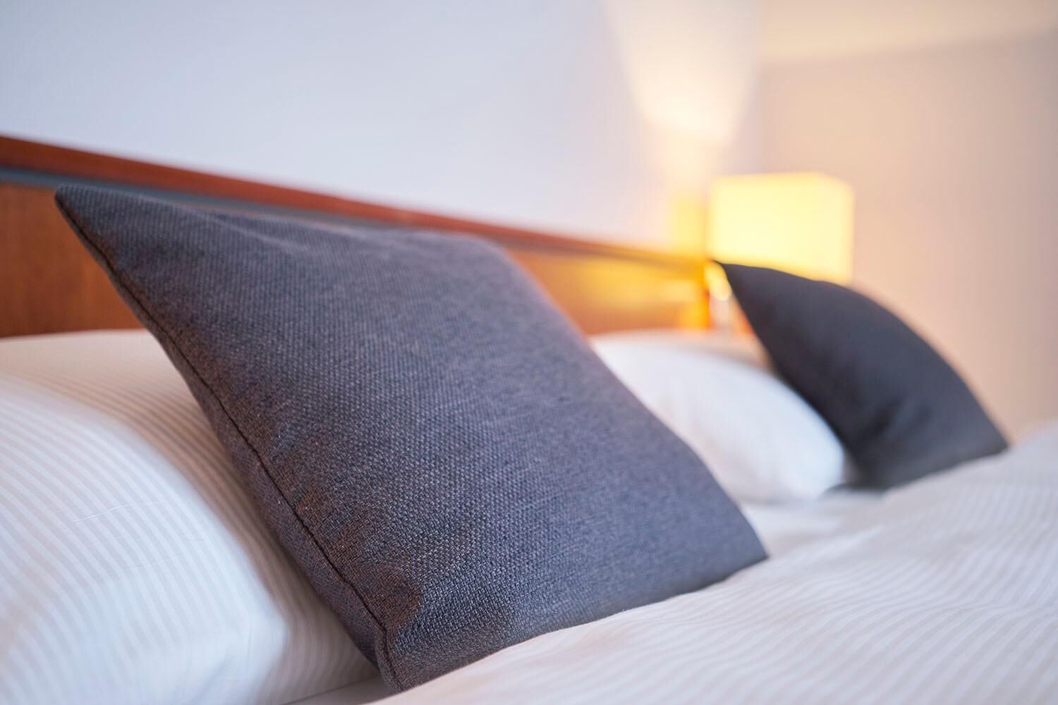 A neatly made bed with white linens and two dark gray pillows.