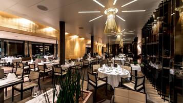 Ein geräumiges Restaurant mit mehreren Tischen und Stühlen, modernen Leuchten und einem klaren, zeitgemäßen Interieur.