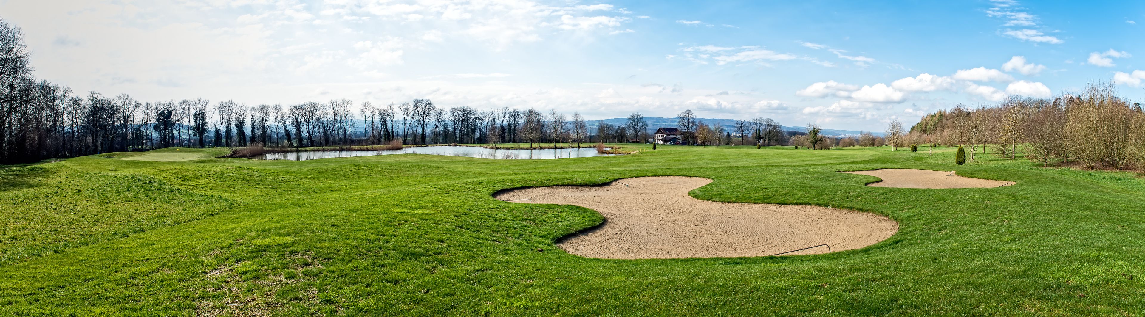 A golf course with sand bunkers, a pond, and a forest in the background.