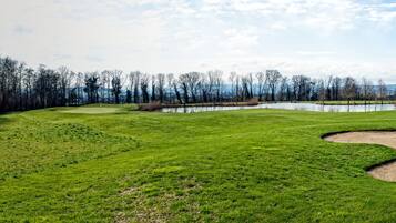 A golf course with sand bunkers, a pond, and a forest in the background.