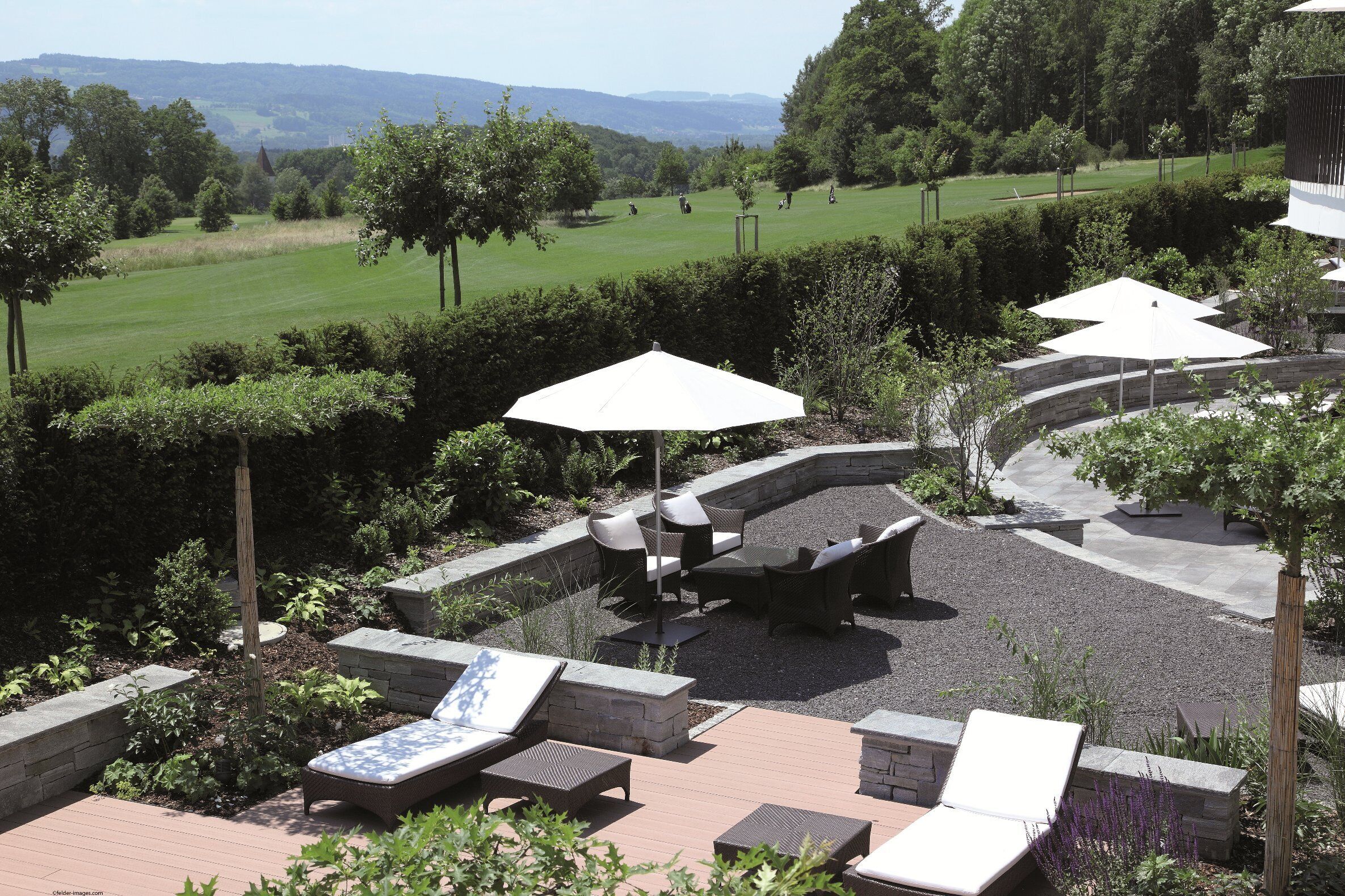 A patio area with lounge chairs, umbrellas, and a view of a golf course.