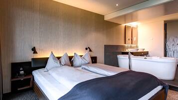 A modern hotel room with a large bed, a built-in bathtub, and a mirror above the sink.