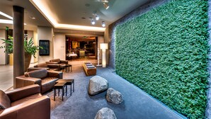 A modern lobby with leather sofas, a green vertical garden, and a reception area.