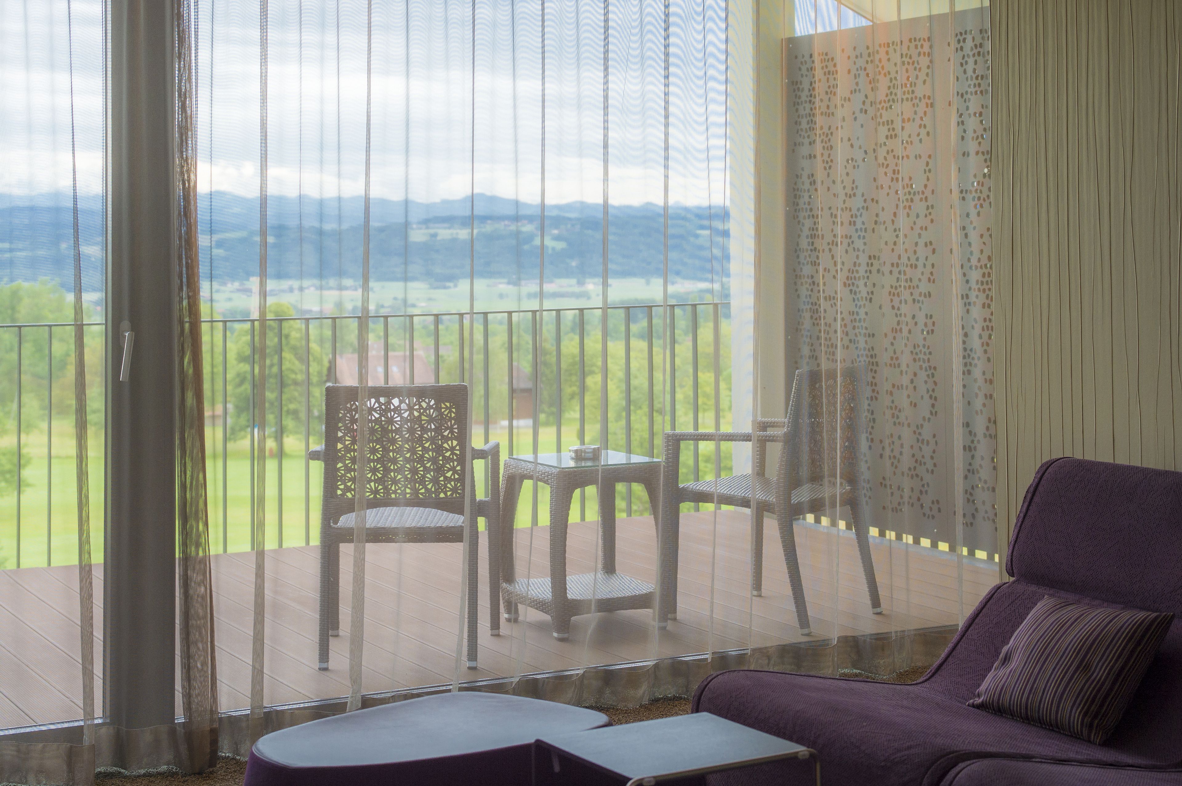 A balcony with wicker furniture, a purple sofa, and a view of a green landscape.