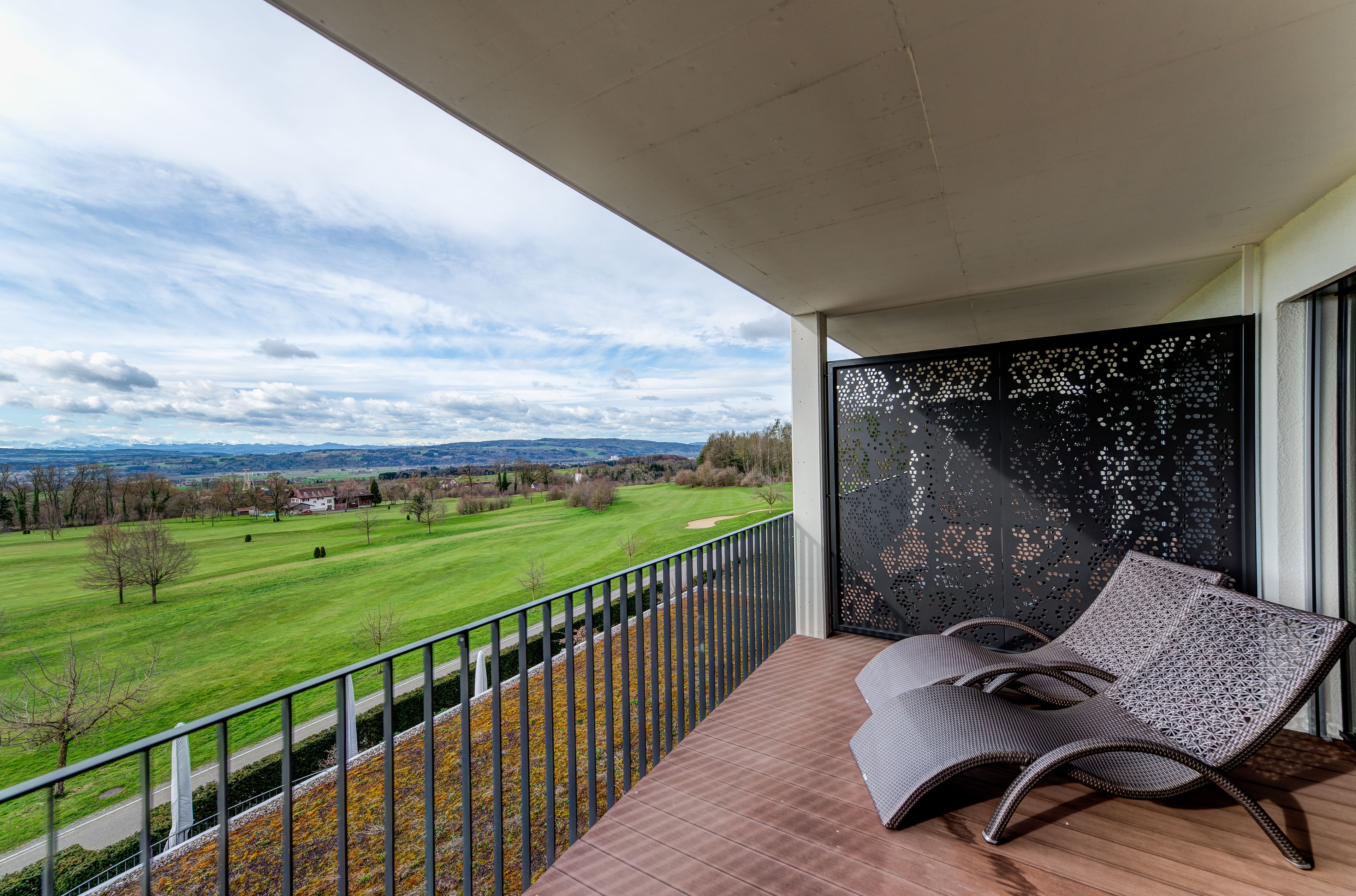 A balcony with a view of a green field and distant hills.