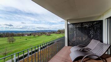 A balcony with a view of a green field and distant hills.