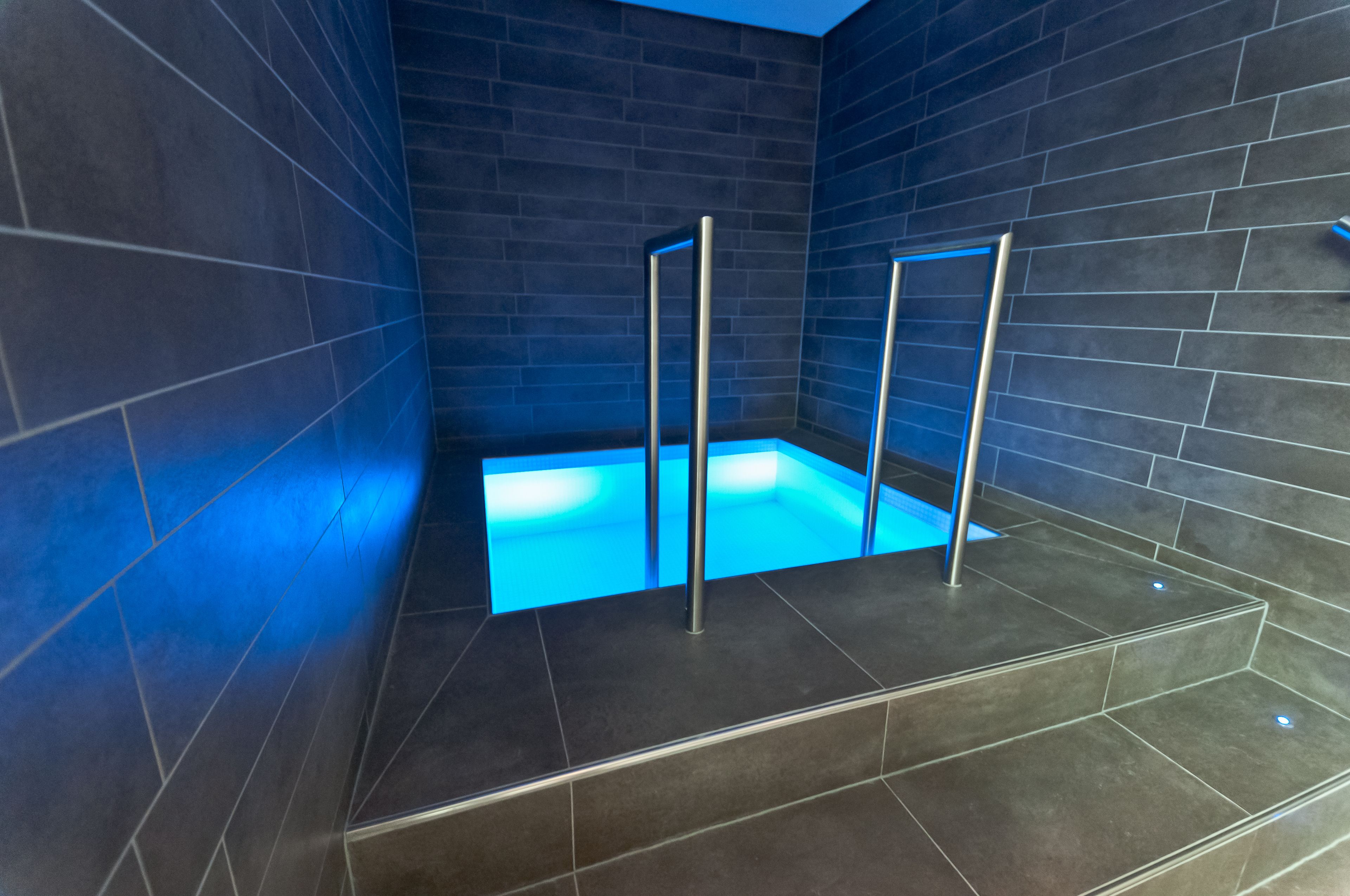 Ein moderner Wellnessbereich mit warmer Bodenheizung, Metallstützen und dunklen Fliesenwänden.
