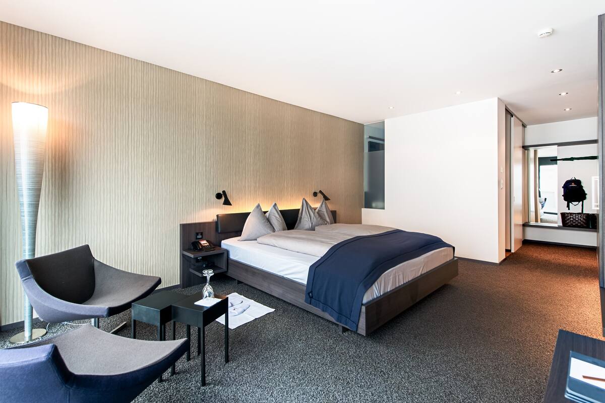 A modern hotel room with a bed, bedside tables, a desk, a chair, and a lamp.