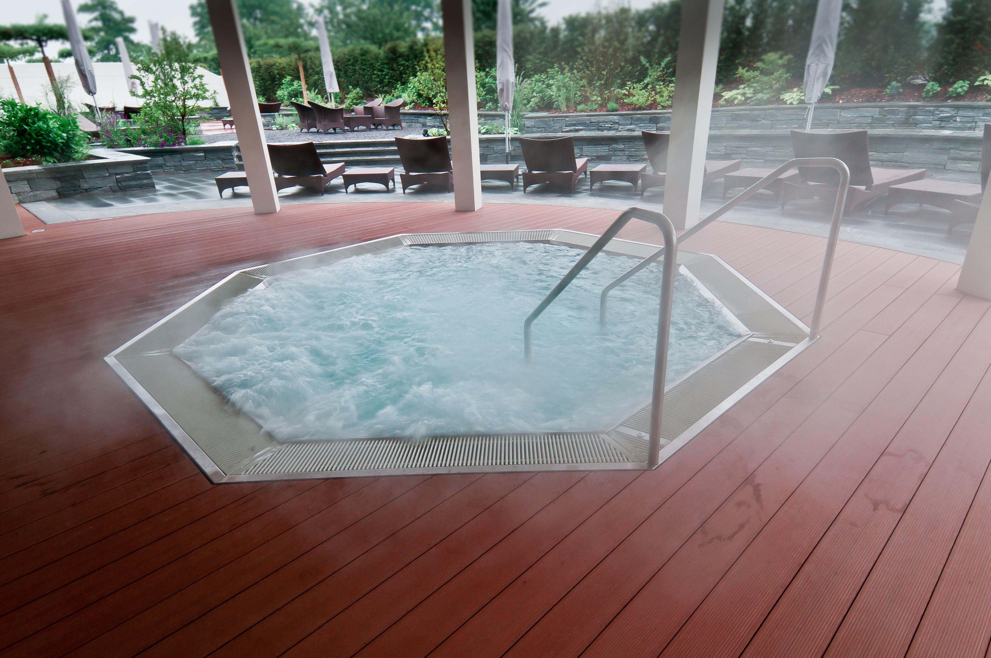 Un bain à remous doté d’une terrasse en bois, entouré de chaises longues et d’un mur en pierre.