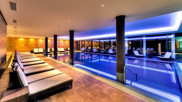 A modern indoor pool area with lounge chairs and a clear view of the pool.