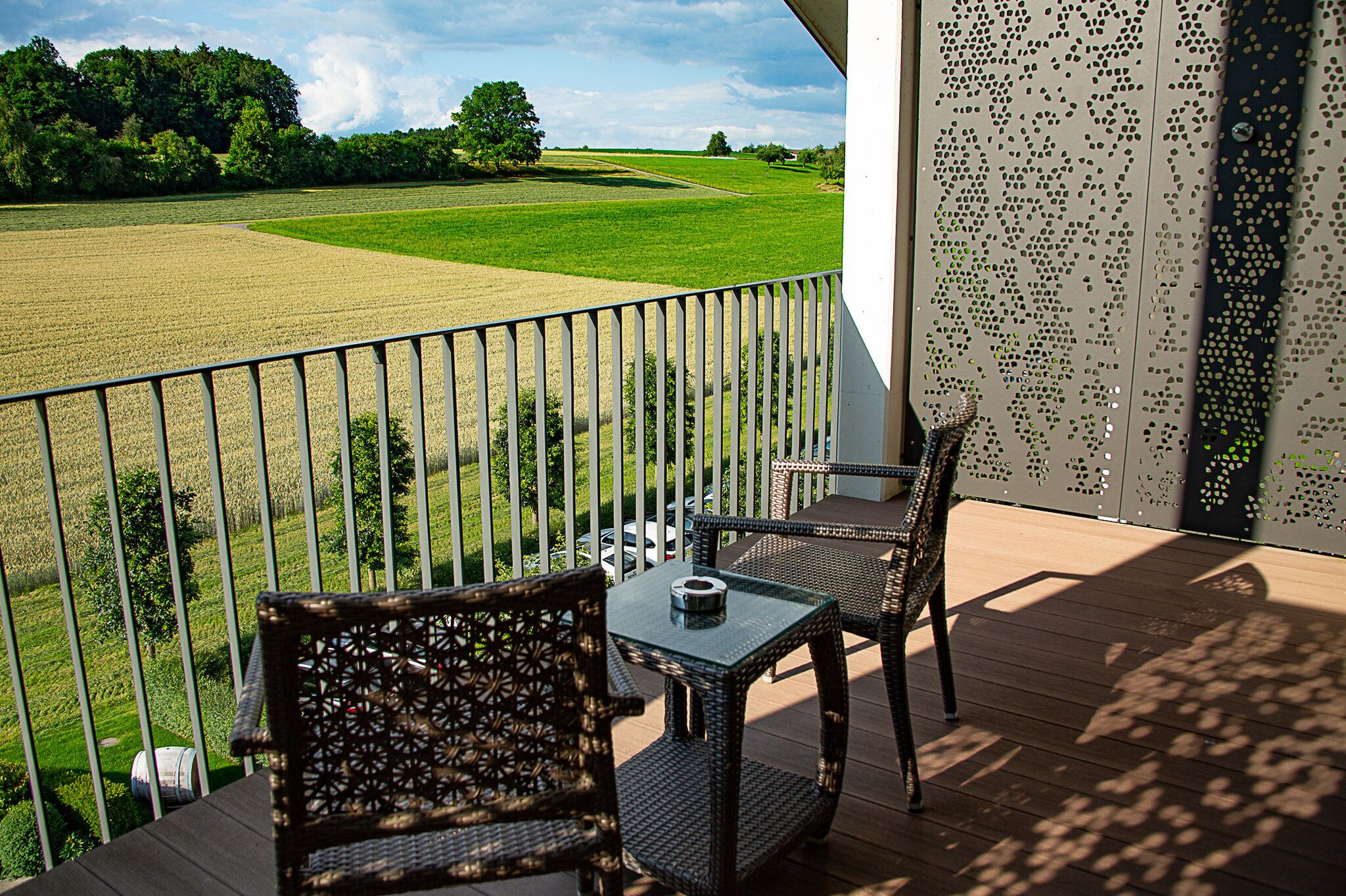 Een balkon met rieten meubilair, een tafel en uitzicht op een groen veld.