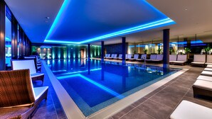 A modern indoor swimming pool with blue ambient lighting, lounge chairs, and a clean, contemporary design.