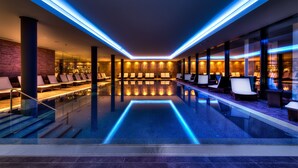A modern indoor pool area with seating and a glass barrier.