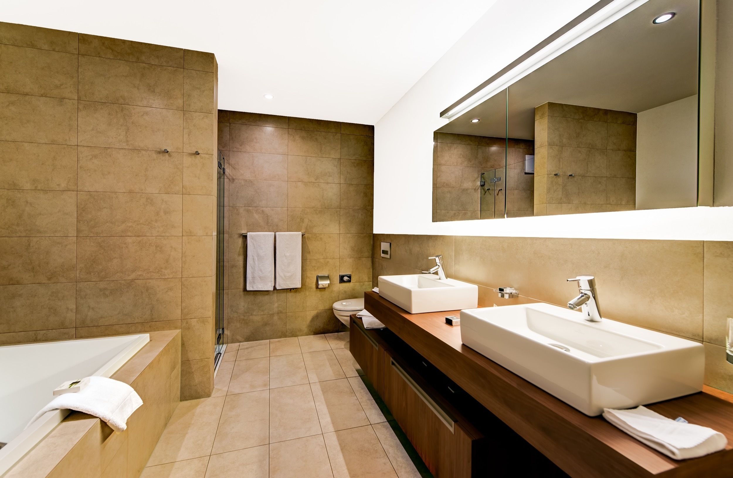 A modern bathroom with a bathtub, two sinks, and a large mirror.