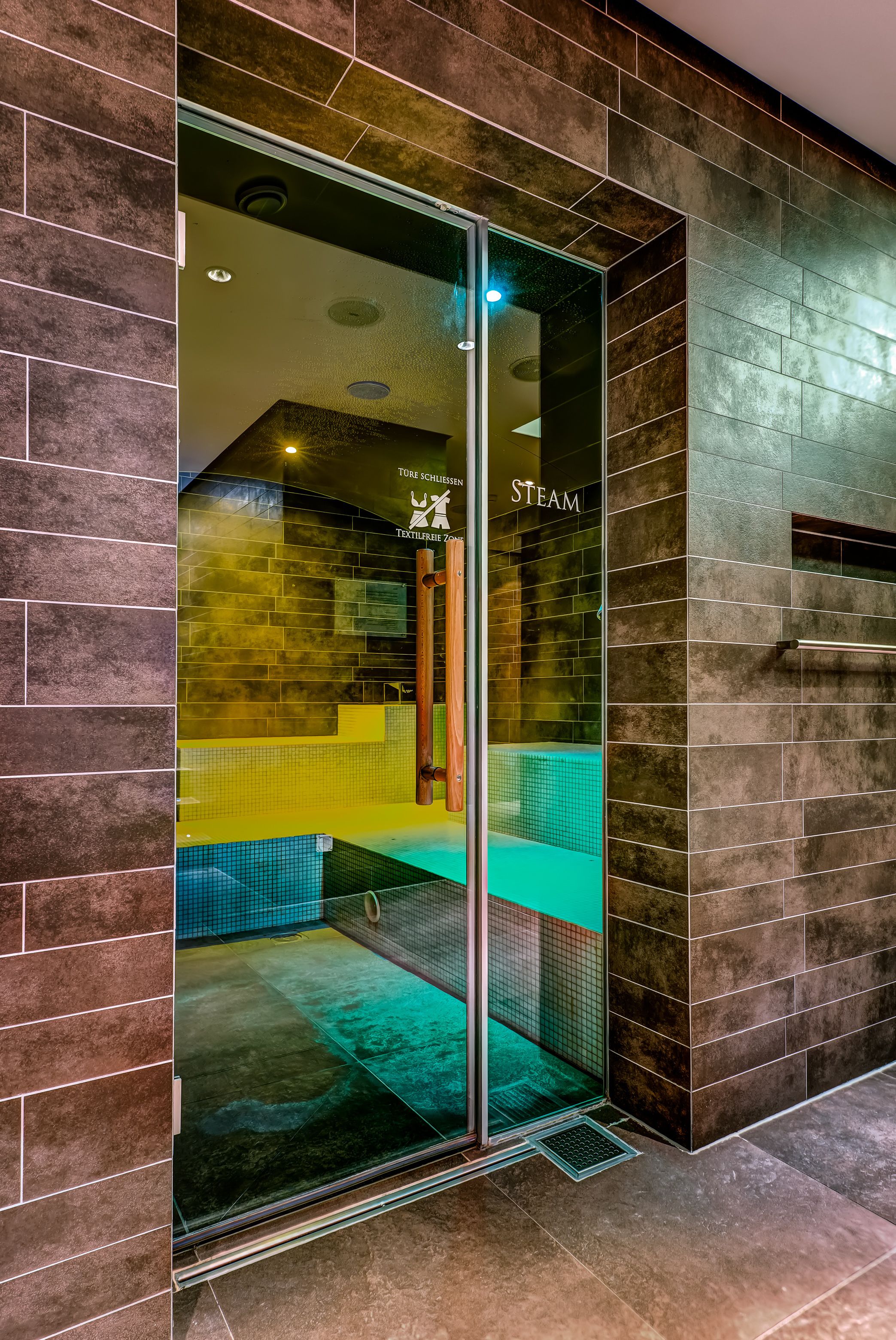 Ein moderner Spa-Bereich mit Glastür, sichtbarer Dampfsauna und gefliesten Innenräumen.