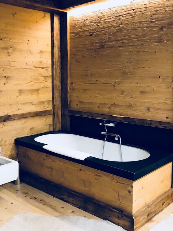 A wooden cabin interior with a bathtub, wooden walls, and a black countertop.