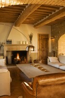 A cozy living room with a fireplace, wooden beams, stone walls, and a leather sofa.