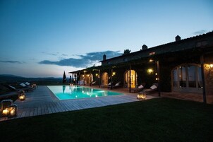 A poolside area with a wooden deck, lounge chairs, and a stone building with arched windows.