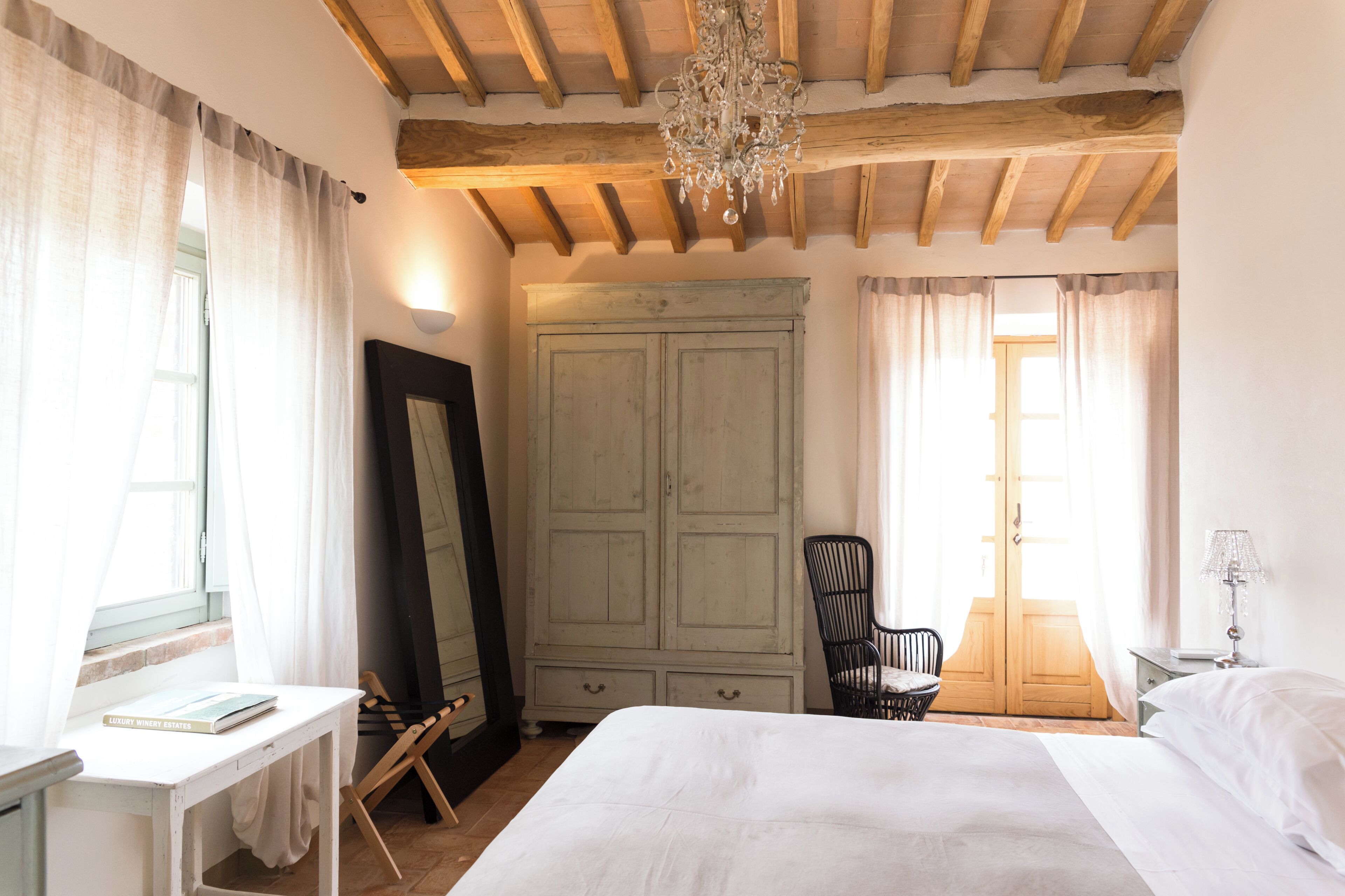 A bedroom with a bed, a desk, a chair, a wardrobe, and a chandelier.
