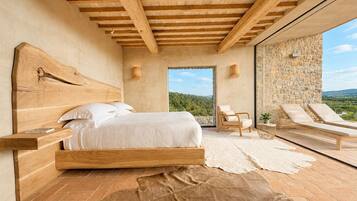 Quarto com cabeceira de madeira, uma cama grande, parede de pedra e vista para o exterior.