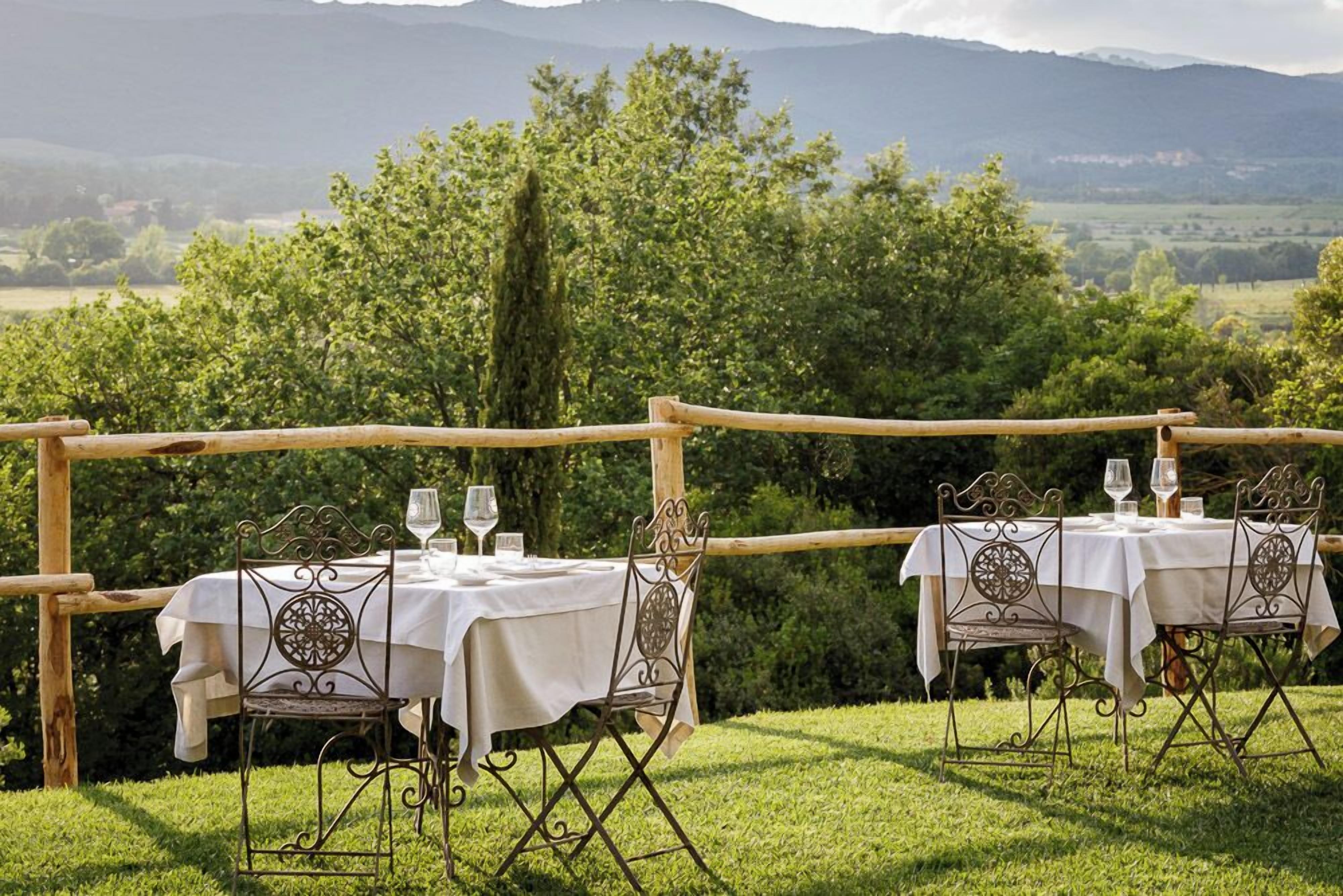 An outdoor dining setup with two tables and chairs, set against a backdrop of greenery and distant mountains.