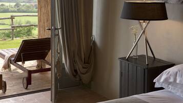 Un dormitorio con cama, mesita de noche, lámpara, silla y vistas al exterior.