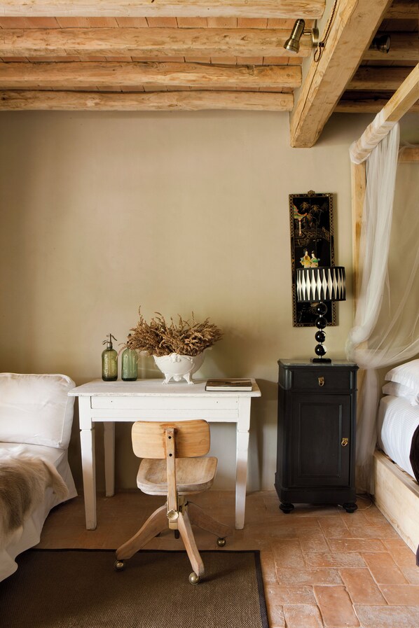 A bedroom with a bed, a desk with a chair, a nightstand, a lamp, and a wall-mounted decoration.
