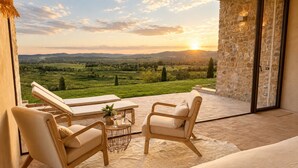 A balcony with a view of a green landscape and a sunset. There are two lounge chairs and a small table with a glass of wine. - Conti di San Bonifacio Wine Resort (Gavorrano)
