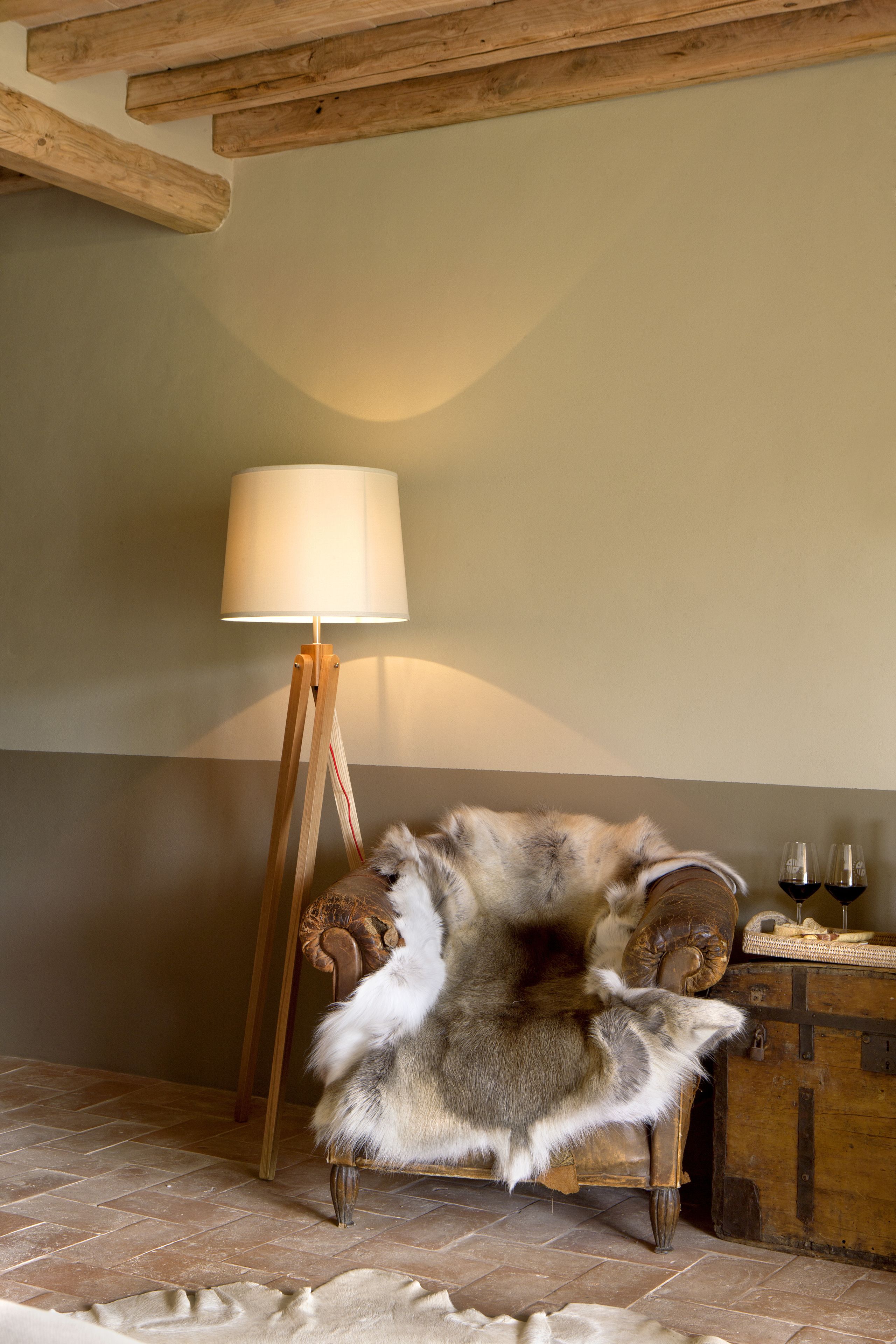 Une pièce avec un plancher en bois, une lampe, un fauteuil en fourrure et un buffet en bois contenant des verres à vin.
