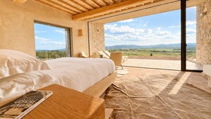 A bedroom with a large bed, a view of the countryside, and a stone wall. - Conti di San Bonifacio Wine Resort (Gavorrano)