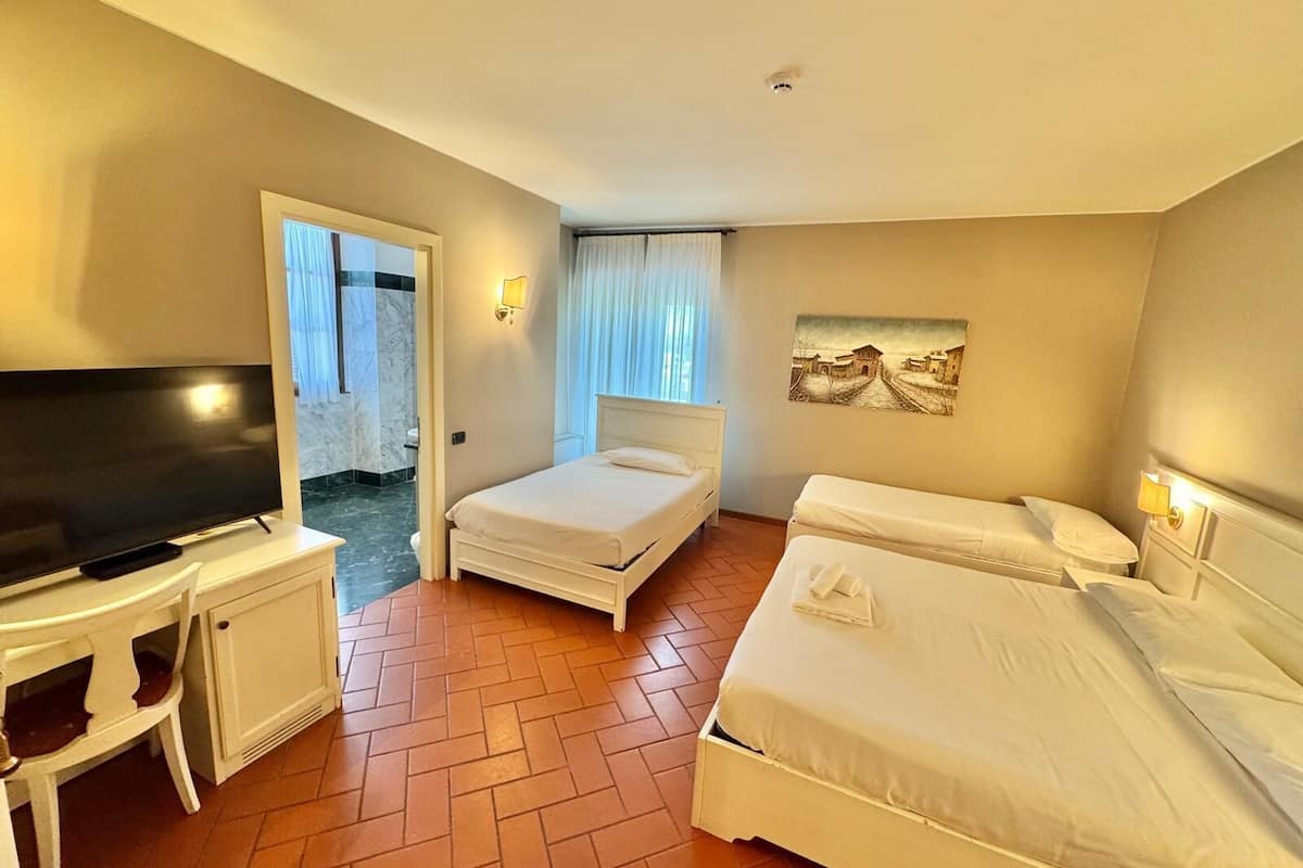 A hotel room with a TV, a desk, two beds, and a bathroom visible through an open door.