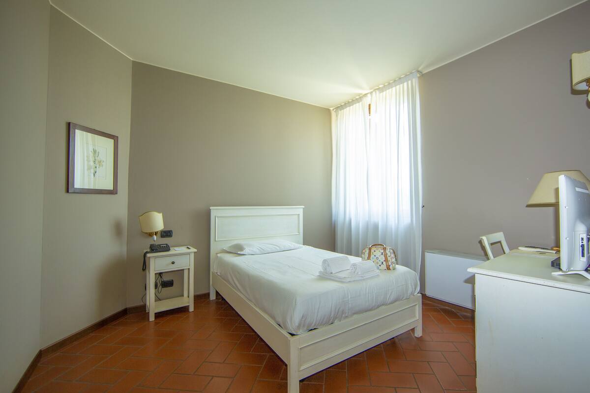 A neatly arranged bedroom with a bed, bedside table, lamp, and a desk with a chair.