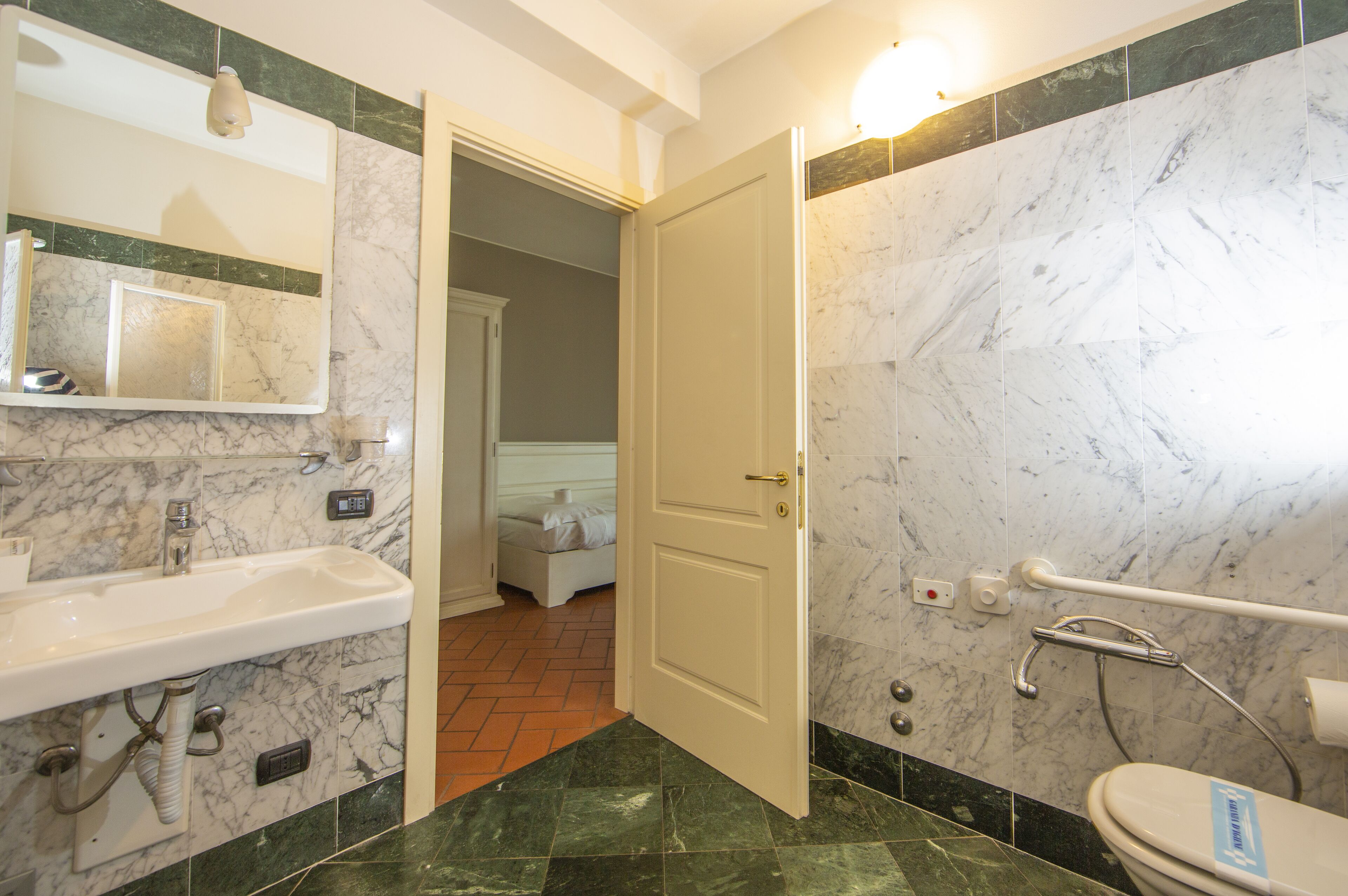 A bathroom with a sink, mirror, toilet, and a door leading to a bedroom.