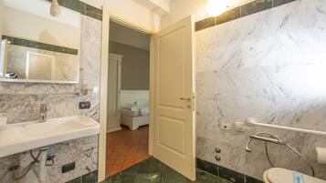 A bathroom with a sink, mirror, toilet, and a door leading to a bedroom.
