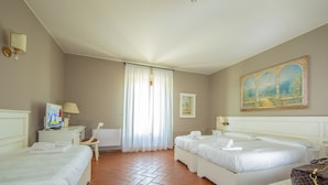 A hotel room with two beds, a desk with a lamp, a chair, a painting on the wall, and a tiled floor. - HC Hotel Il Gelso Pontevico (Pontevico)