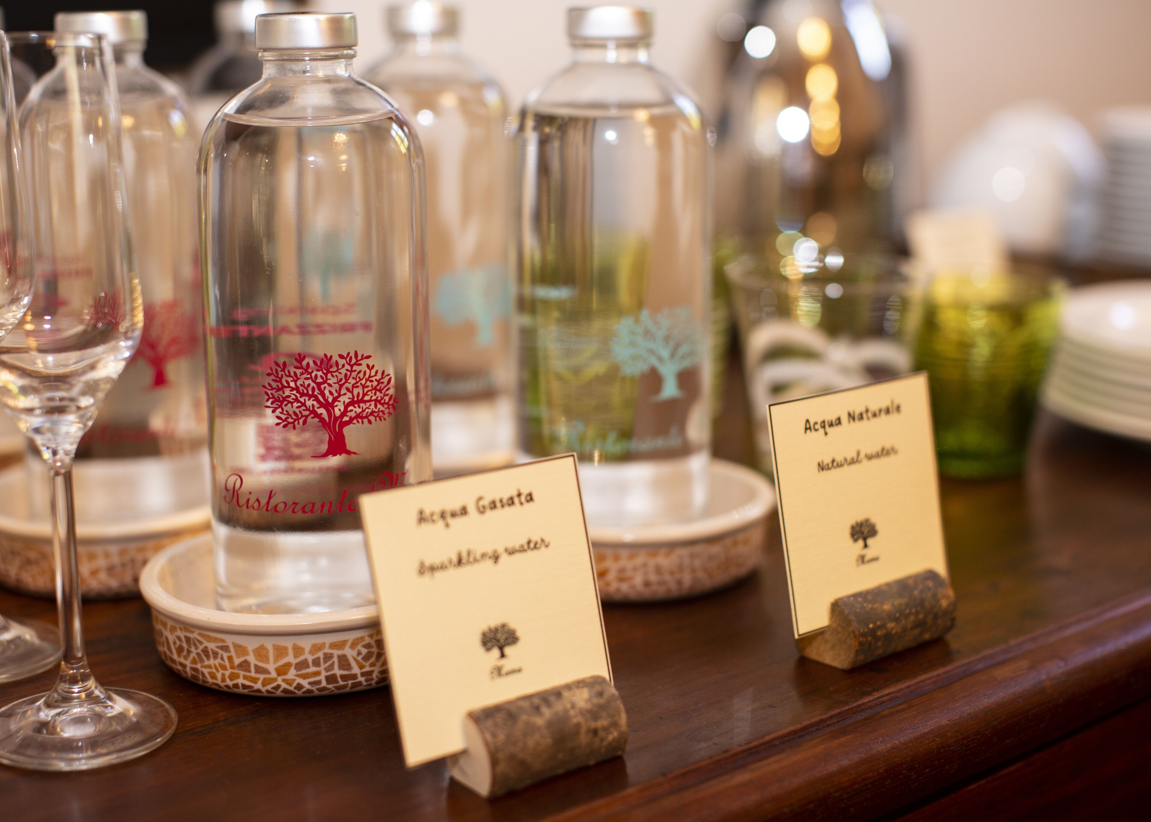 Una exposición de botellas de vidrio con etiquetas y un cartel que indica 'Acqua Gasata' agua con gas.
