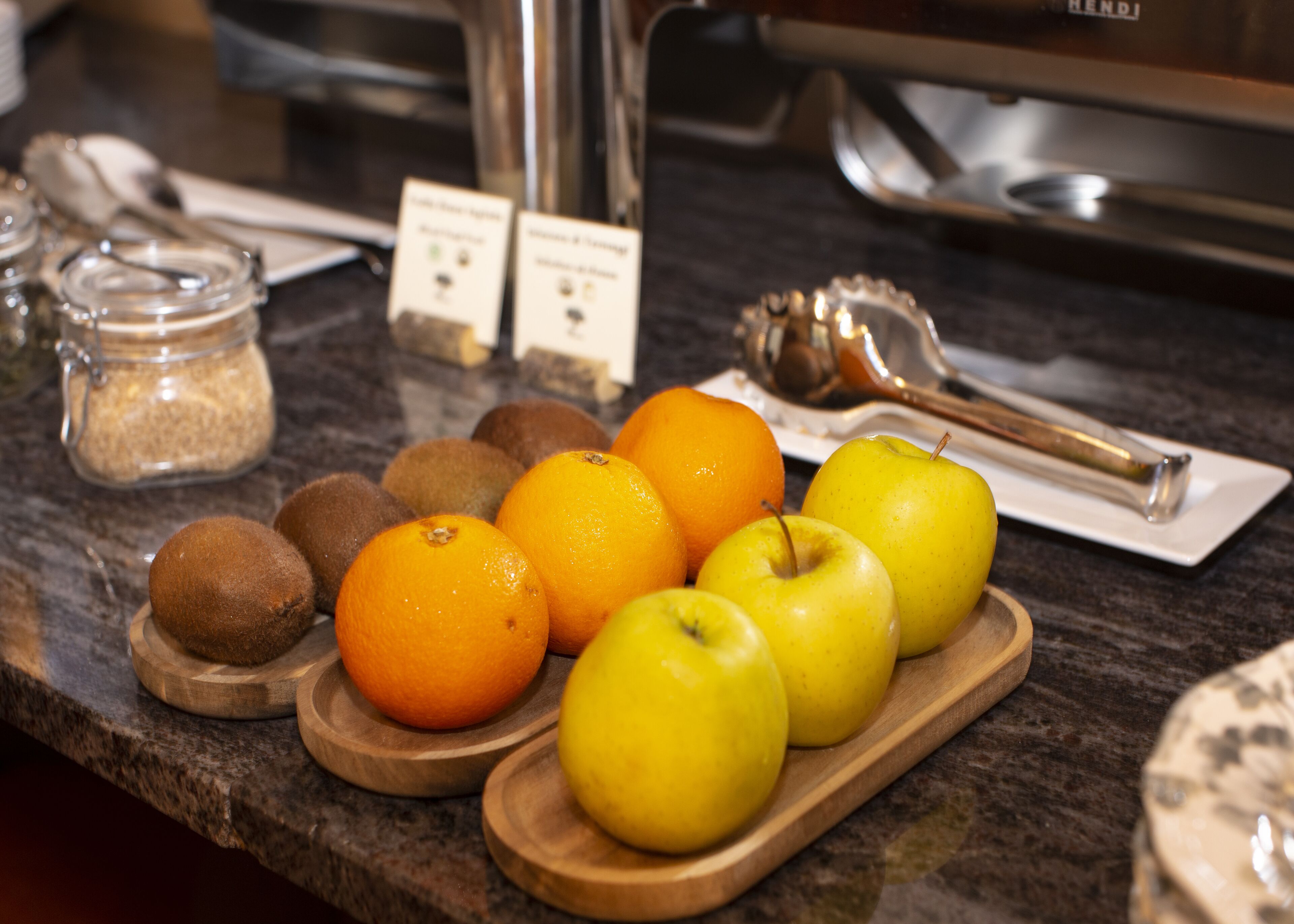 A wooden tray with apples and oranges on a kitchen counter.