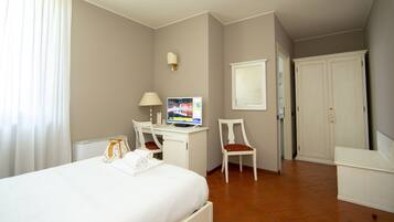 Habitación de hotel con cama, escritorio con computadora, silla, armario y ventana con cortinas.