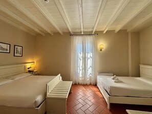 Habitación de hotel con dos camas, una mesita de noche con lámpara, luz empotrada en la pared y ventana con cortinas traslúcidas.