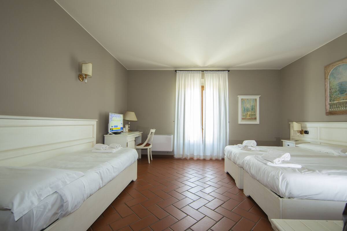 A hotel room with two beds, a desk with a computer, a chair, and a window with curtains.