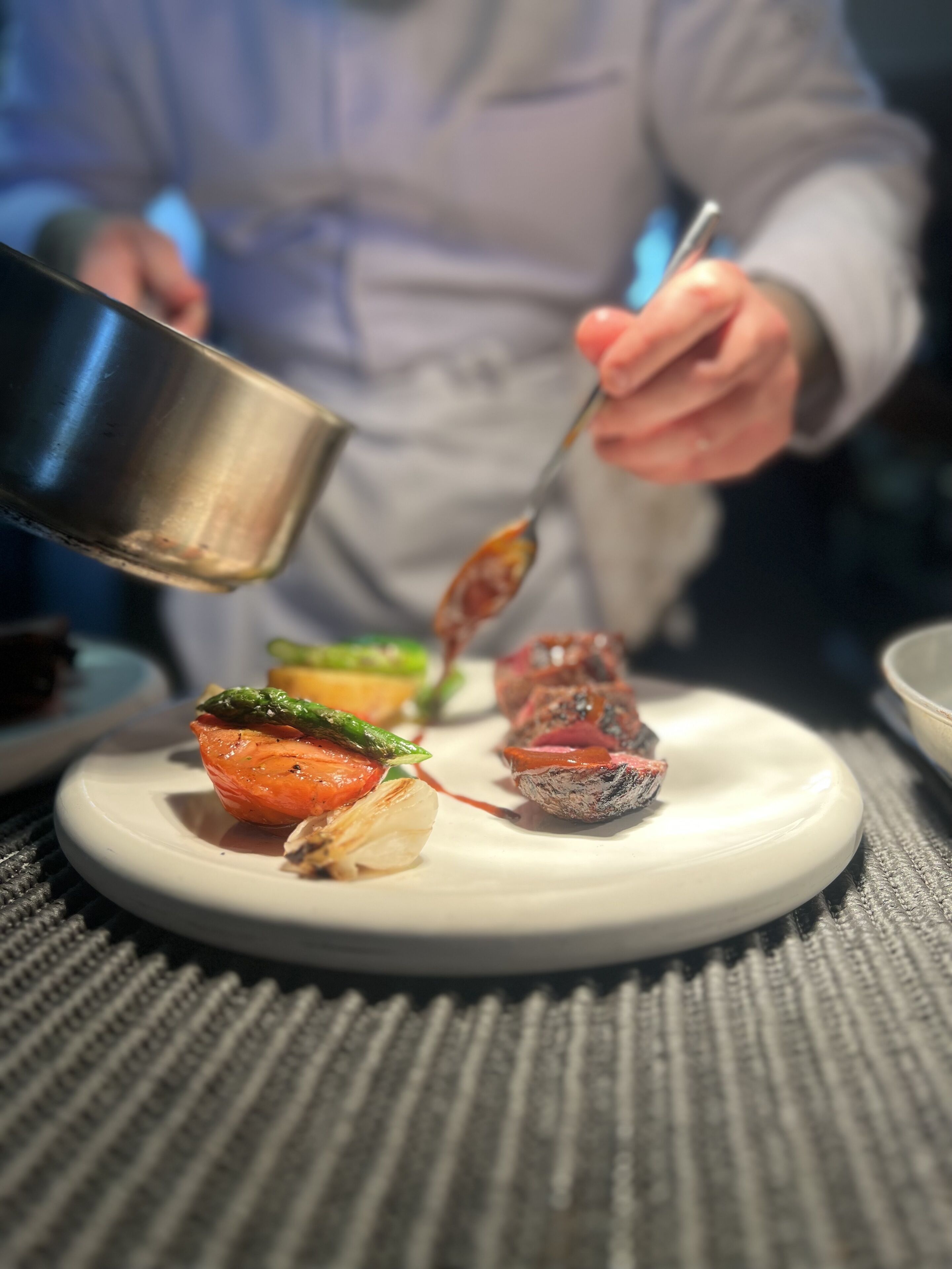 A chef preparing a dish with a spoon and a metal container on a white plate.