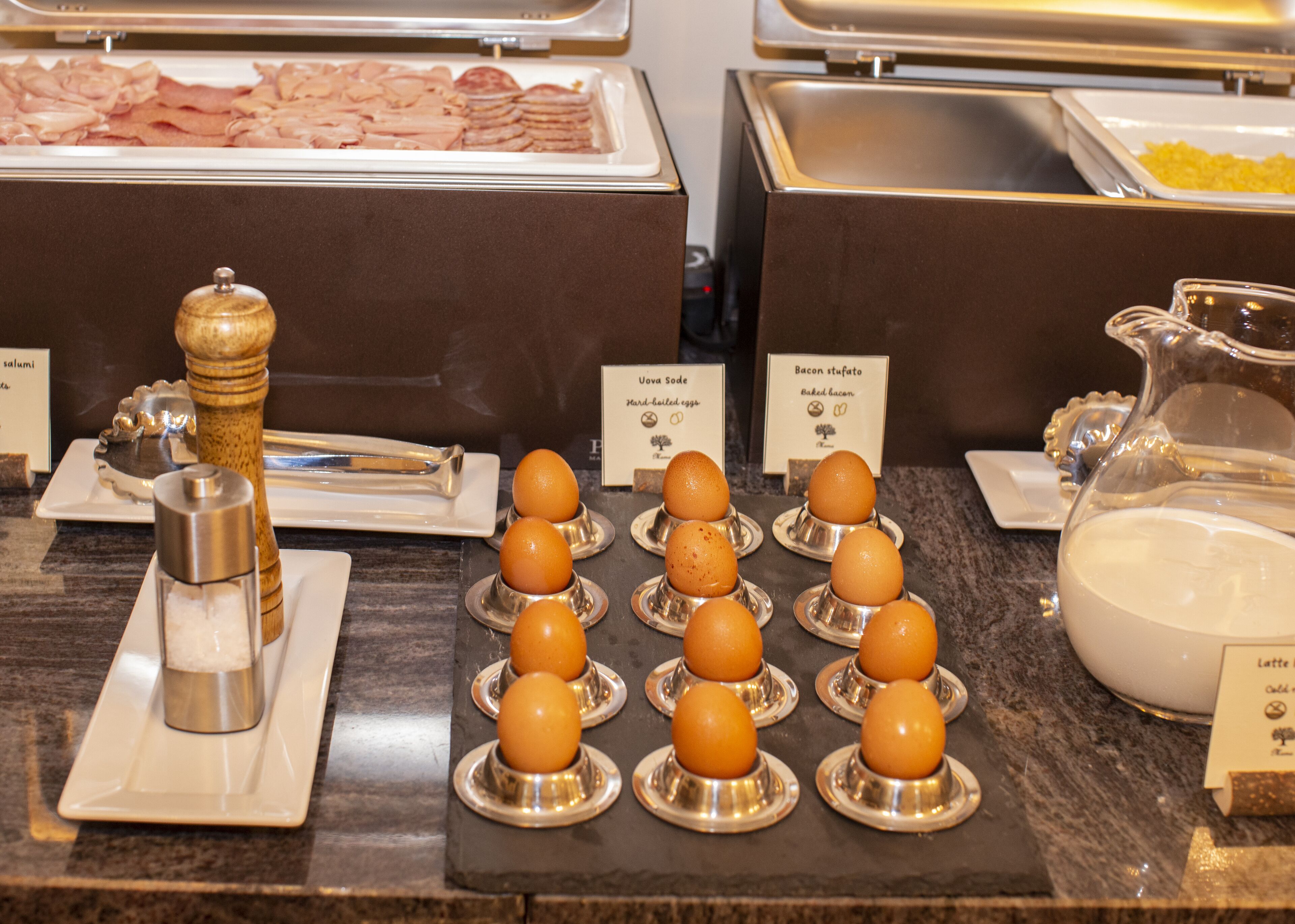 A buffet with various food items including eggs, bacon, and a pitcher of milk.