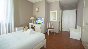A hotel room with a bed, a desk with a computer, a chair, and a small table with a lamp.